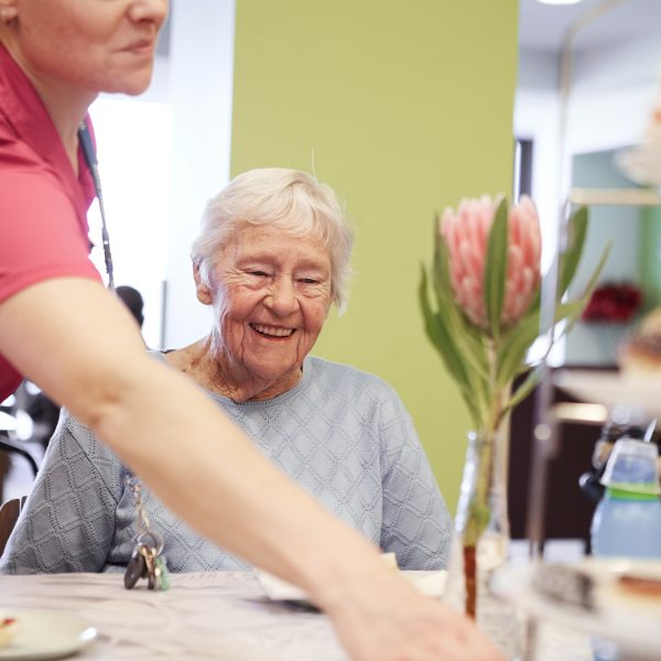 A smiling resident sitting at a table while a caregiver places a plate in front of them at Mercy Health Bethlehem Home for the Aged in Bendigo.